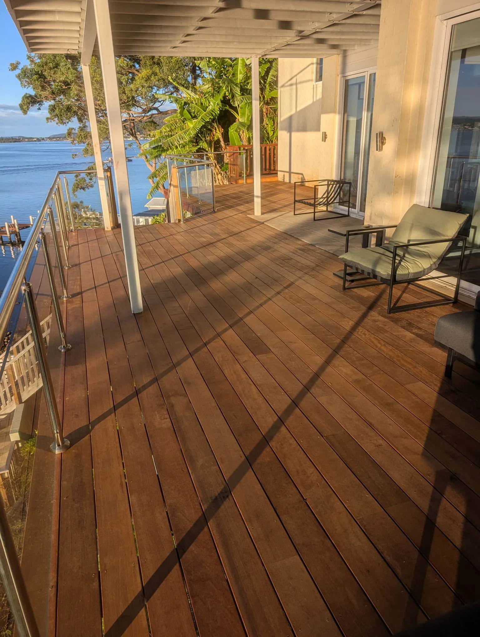 A newly built merbau deck under a verandah, with a glass balustrade and water views