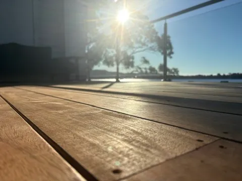 A timber deck catching low winter sun, with a glass balustrade and water views